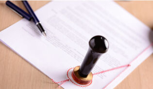Na stole znajduje się poświadczony notarialnie dokument, długopisy i pieczęć-PL