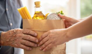 Руки передають паперовий пакет з продуктами (макарони, олія, консерви) літній людині - символ продуктової допомоги FEPŻ для українців у Польщі.