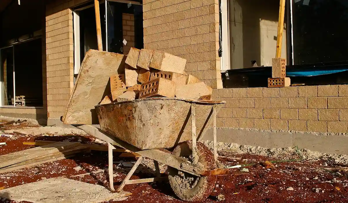 Біля будинку стоїть тачка, наповнена цеглою, готова до будівельних або ландшафтних робіт.