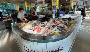 Tętniący życiem stoisko z rybami w restauracji, wokół którego zgromadziło się kilka osób, przeglądających asortyment świeżych owoców morza.