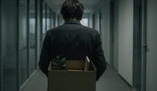 Pracownik niesie karton z rzeczami osobistymi korytarzem biurowym po zwolnieniu z pracy